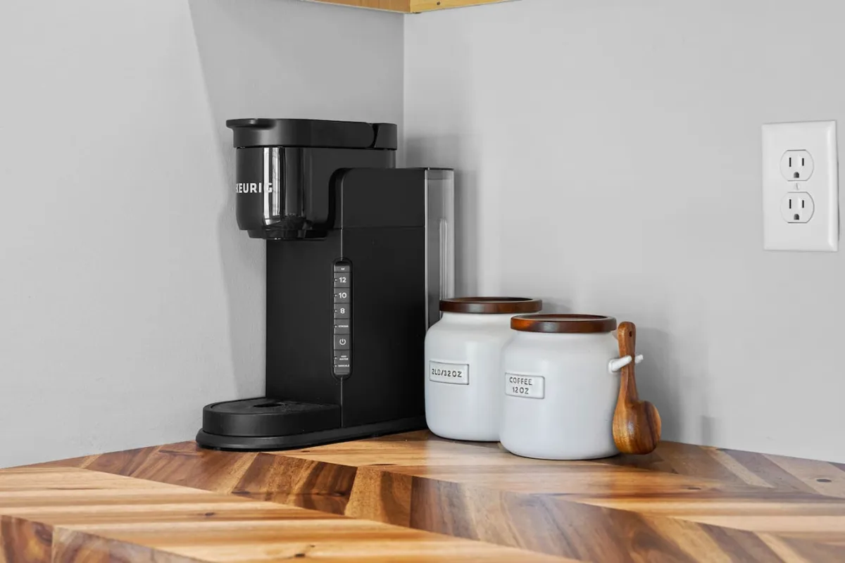 A welcoming coffee corner featuring a coffee maker, ceramic jars, and attractive wooden accents. The setup invites guests to start their day comfortably, emphasizing both style and practicality. The inviting mood enhances the appeal for travelers looking to enjoy simple routines in a stylish setting.