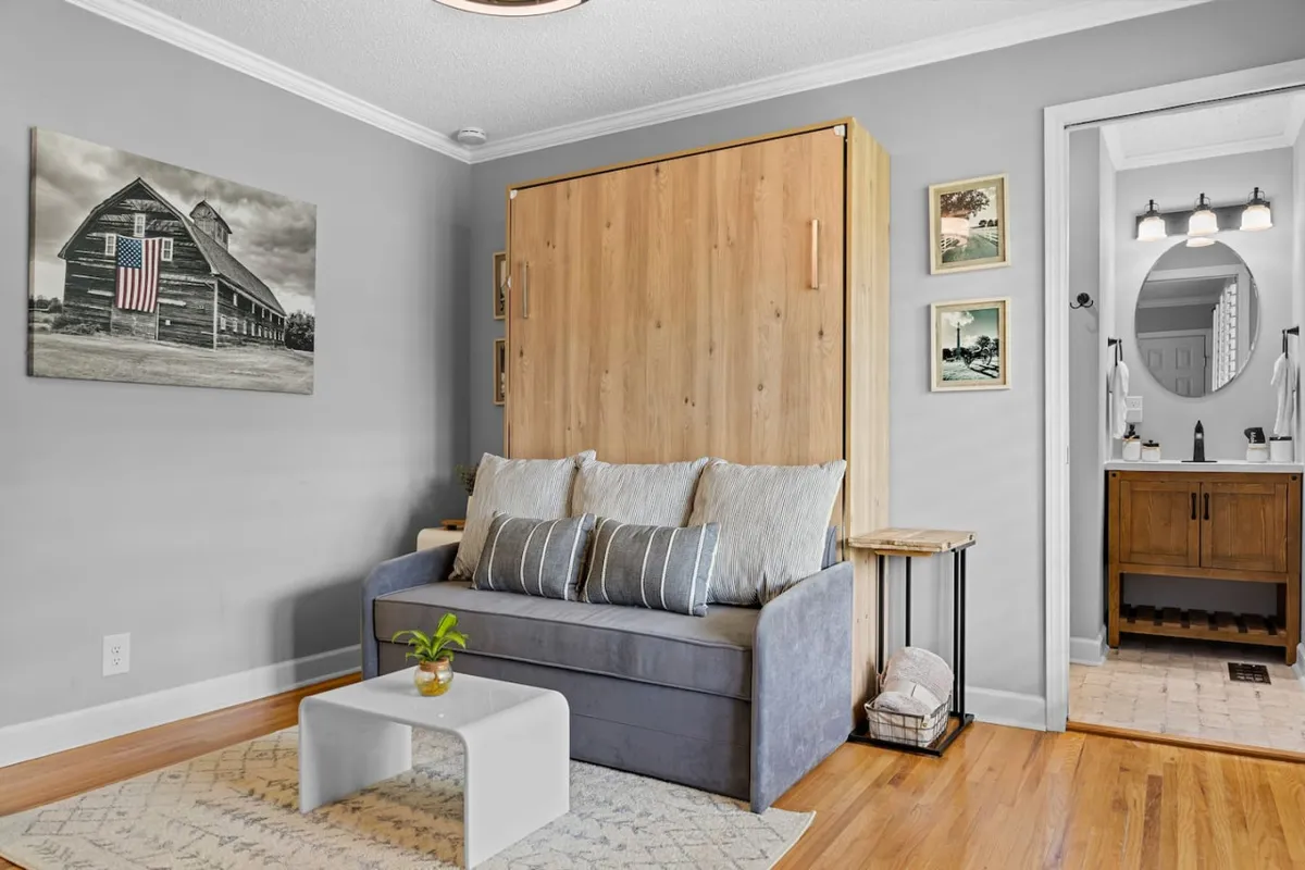 A comfortable, homely living area featuring a sofa bed, wall art, and a coffee table. The soft lighting and inviting arrangement create a tranquil environment, ideal for reading, journaling, or reflecting in solitude. Subtle personal touches and a calm atmosphere evoke a sense of creative retreat.