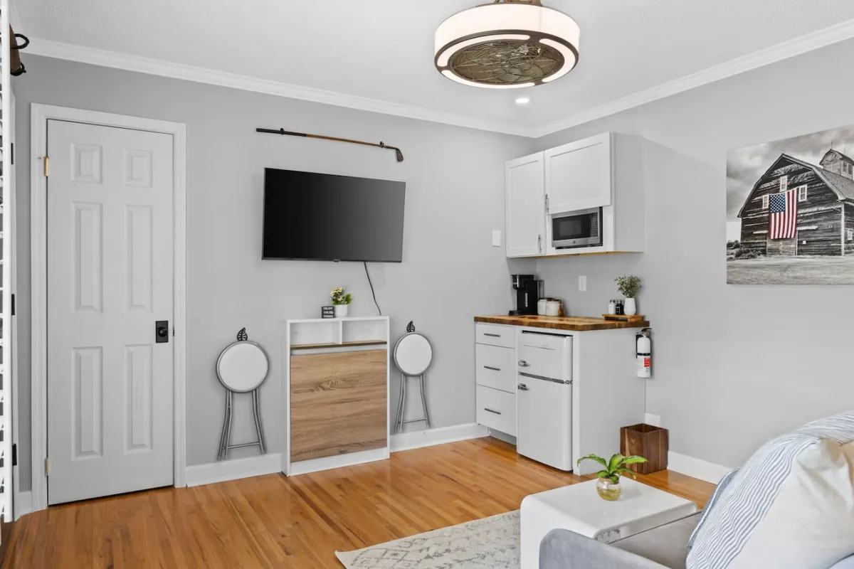 This image showcases a comfortable living area with a visible television, a compact kitchenette, and a striking piece of barn-themed artwork. The space exudes a cozy, welcoming vibe suitable for socializing, sharing a meal, or unwinding with a movie after a day out.