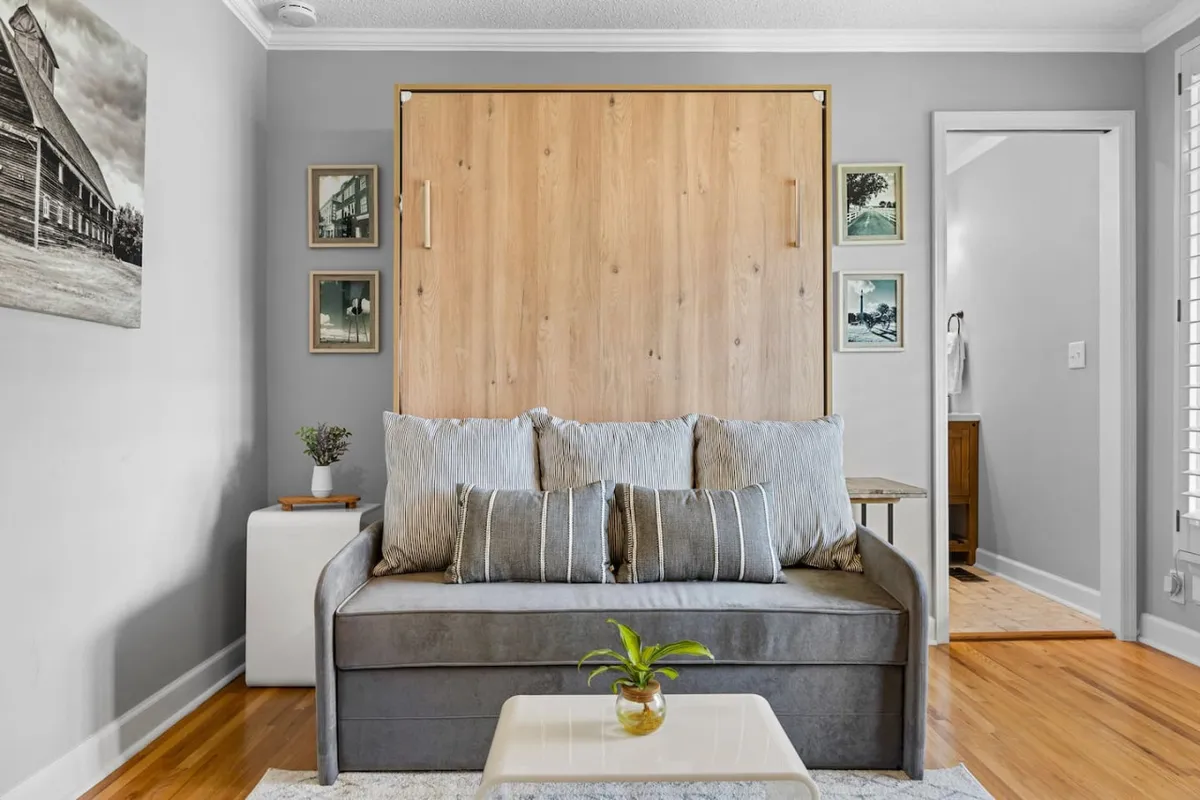 A closer look at the living area reveals the murphy bed, plush sofa, decorative pillows, side table, and framed pictures. The cozy atmosphere is accentuated by soft textures and intentional decorating, ideal for intimate moments or relaxation.