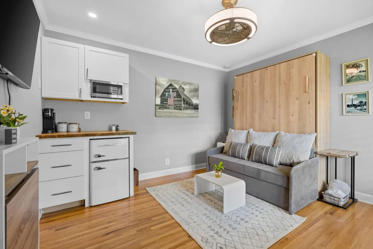 This image showcases the studio living area, featuring a murphy bed, a comfortable sofa, a coffee table, and a kitchenette. The décor is a blend of cozy and modern elements, with carefully arranged furnishings that make the space inviting and functional. The scene suggests a space perfect for relaxing, entertaining, or unwinding after a long day.